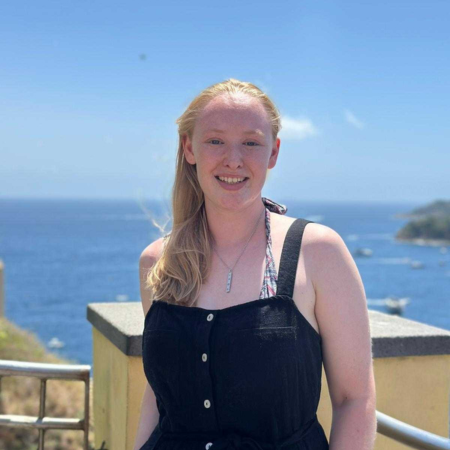 Emily is standing with the sea in the background.